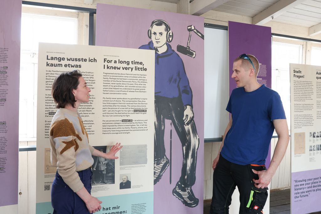Kelsey Snook und Jakob Feisthauer bei der Eröffnung der Ausstellung vor der Ausstellungstafel über den Urgroßvater von Jakob, Heinrich Feisthauer. April 2026, Foto: Karsten Schirmer