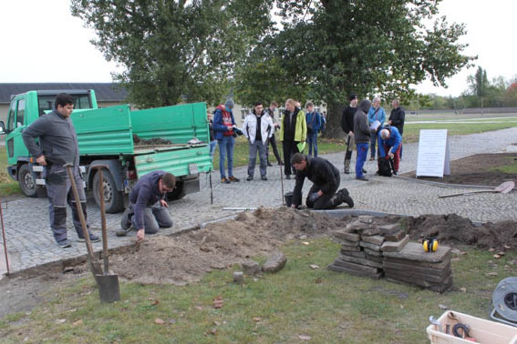 Auszubildende setzen im Bereich der Häftlingswäscherei neue Bordsteine.